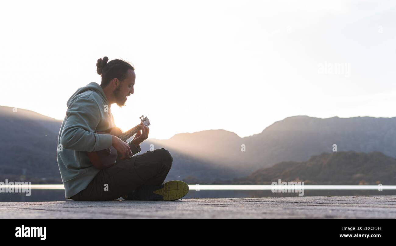 Young man singing while playing ukulele on promenade during sunny day Stock Photo