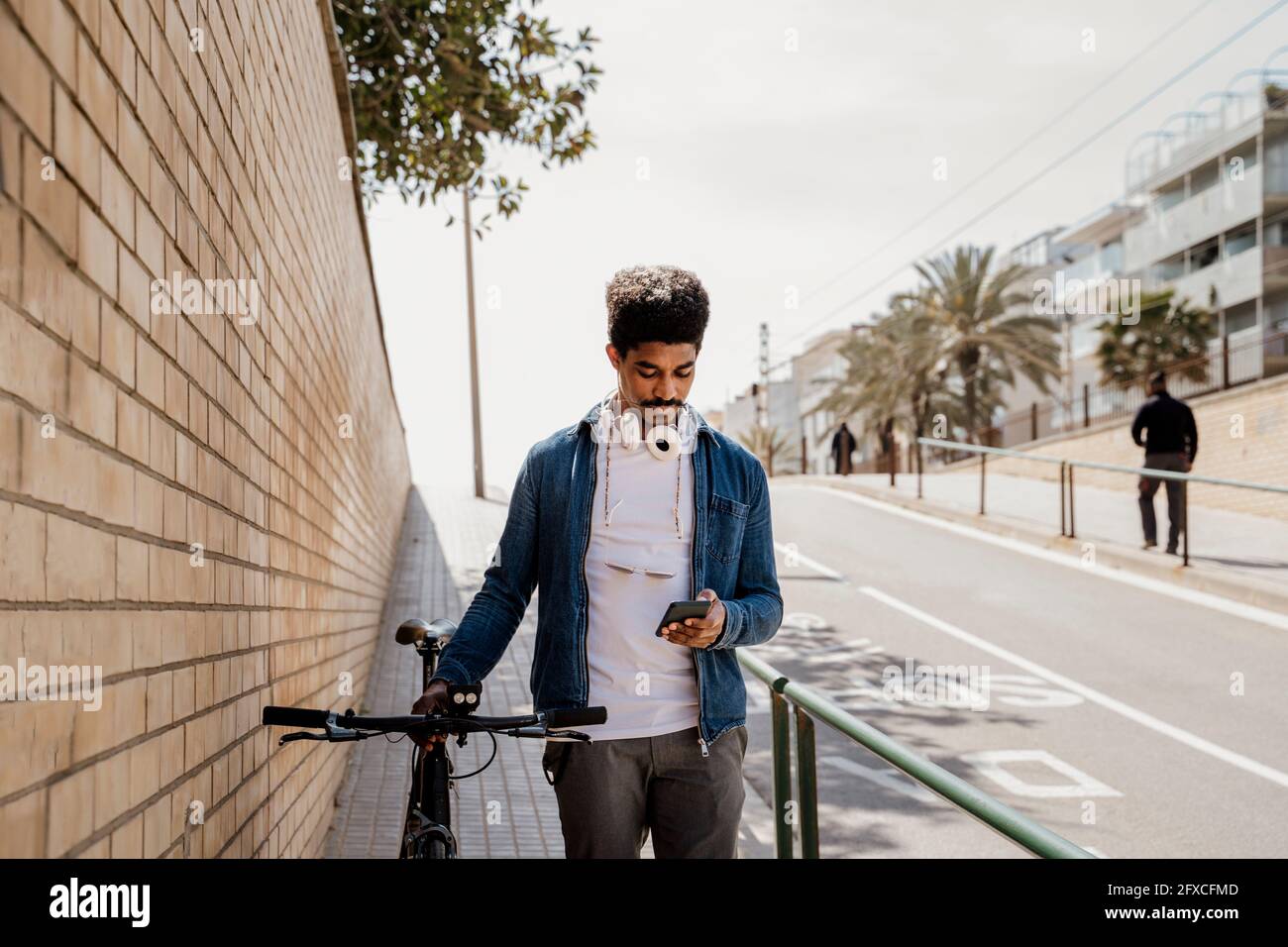 Handsome man using mobile phone while standing with bicycle on footpath Stock Photo