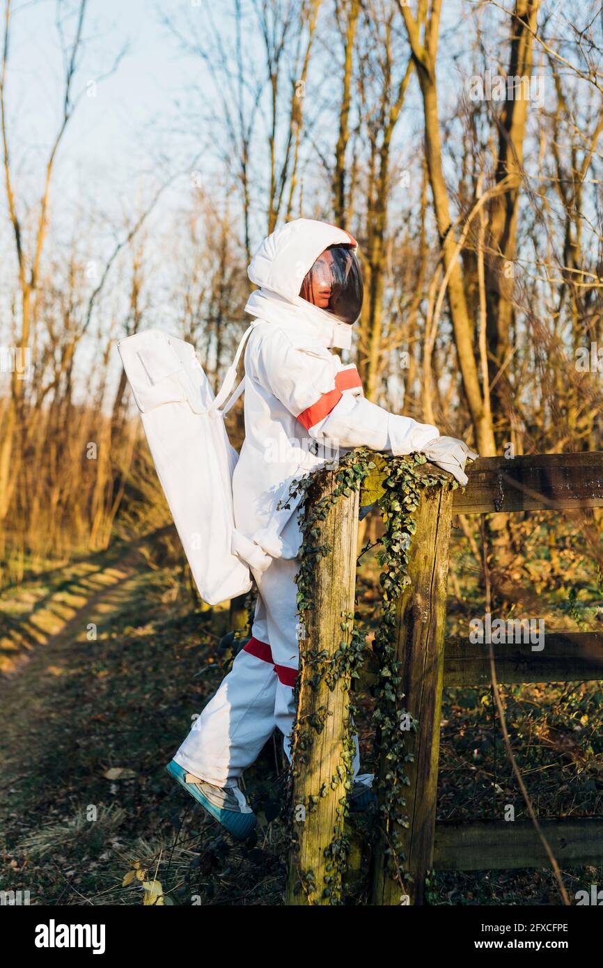 Young female astronaut in space suit and helmet standing by railing in ...