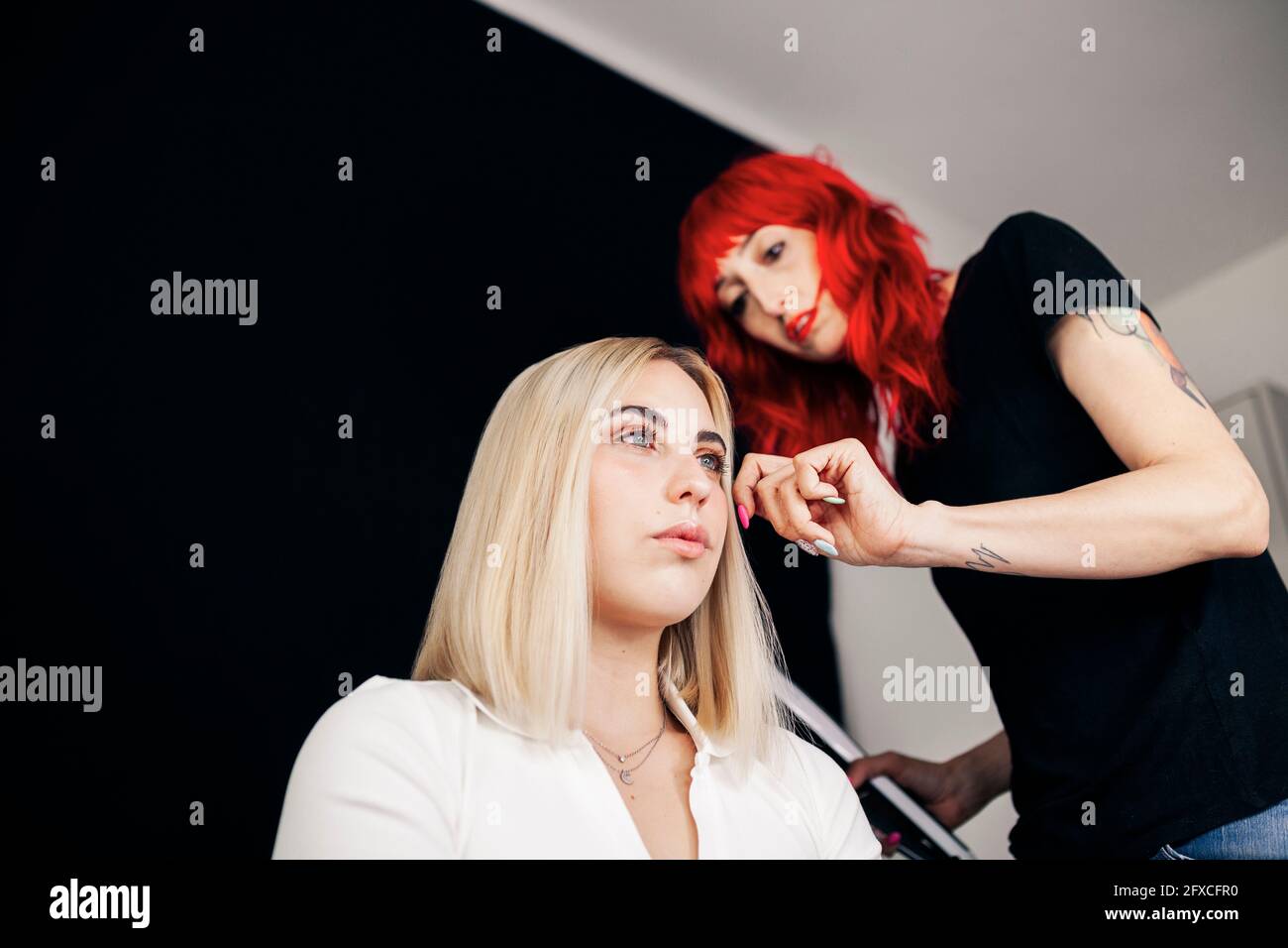 Dyed haired hairstylist adjusting female model's hair at studio Stock Photo