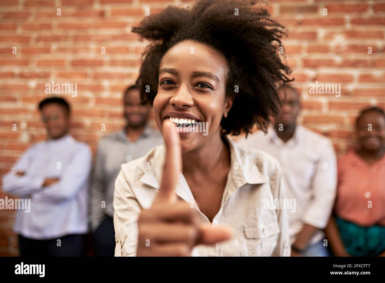 Cheerful businesswoman showing index finger with colleagues in background at office Stock Photo