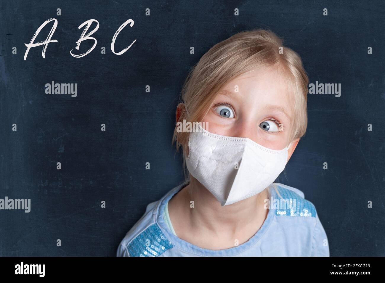 Girl with crossed eyes wearing face mask against black background with alphabets Stock Photo
