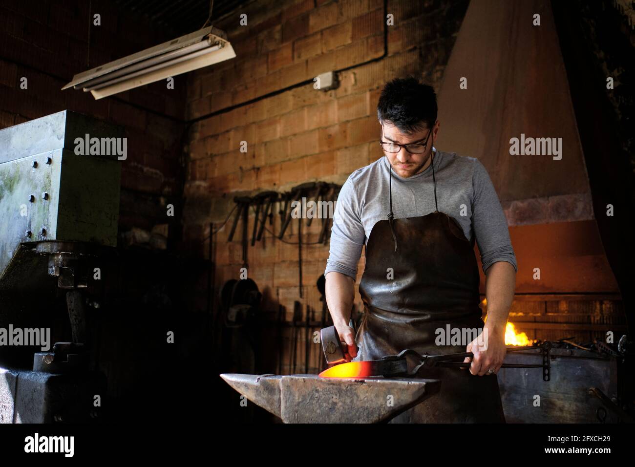 Craftsman hitting overheated metal on anvil at workshop Stock Photo