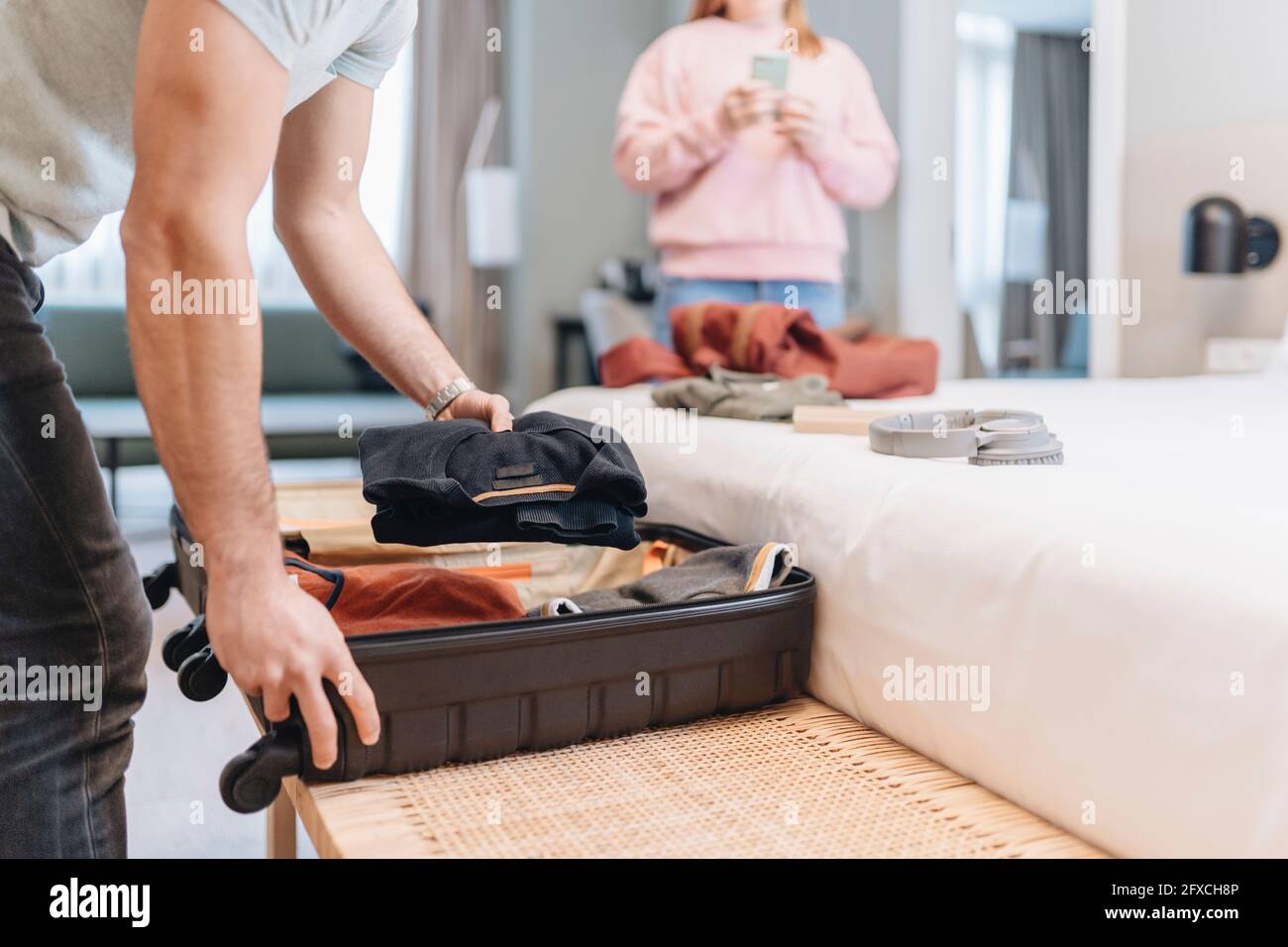 Man removing clothes from suitcase with woman in background at hotel Stock Photo