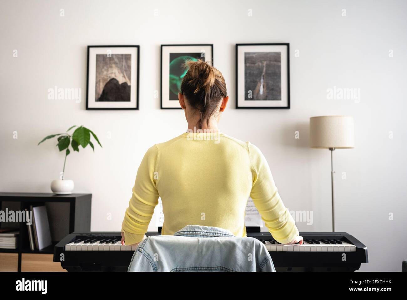 Mid adult woman learning piano in front of picture frame at home Stock Photo