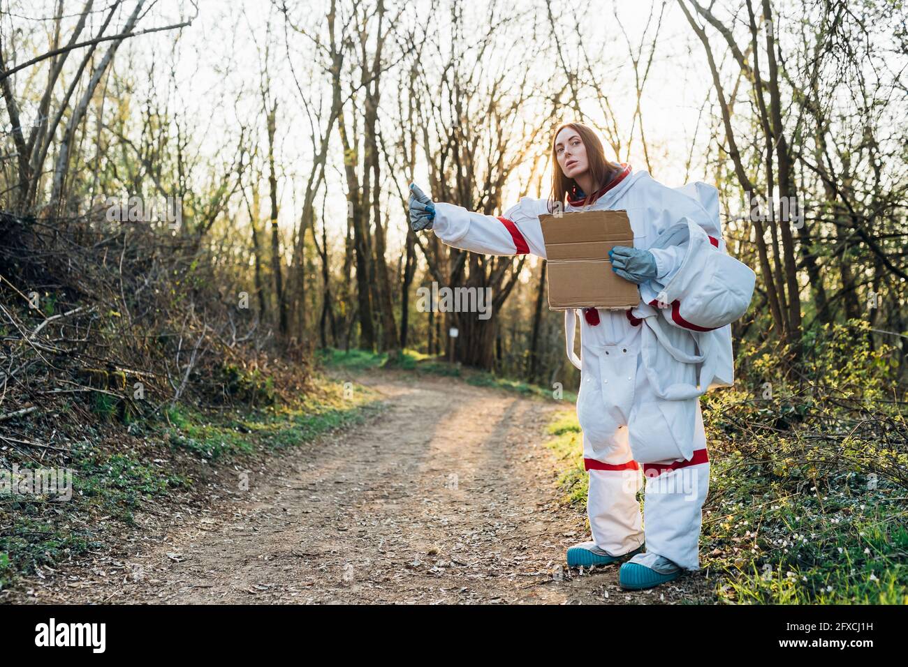 Female astronaut in space suit gesturing while holding cardboard on dirt road Stock Photo