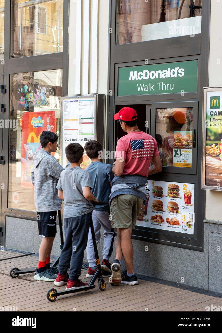 Man and boys with scooters at McDonald's Walk Thru collection point window in Sofia, Bulgaria Stock Photo