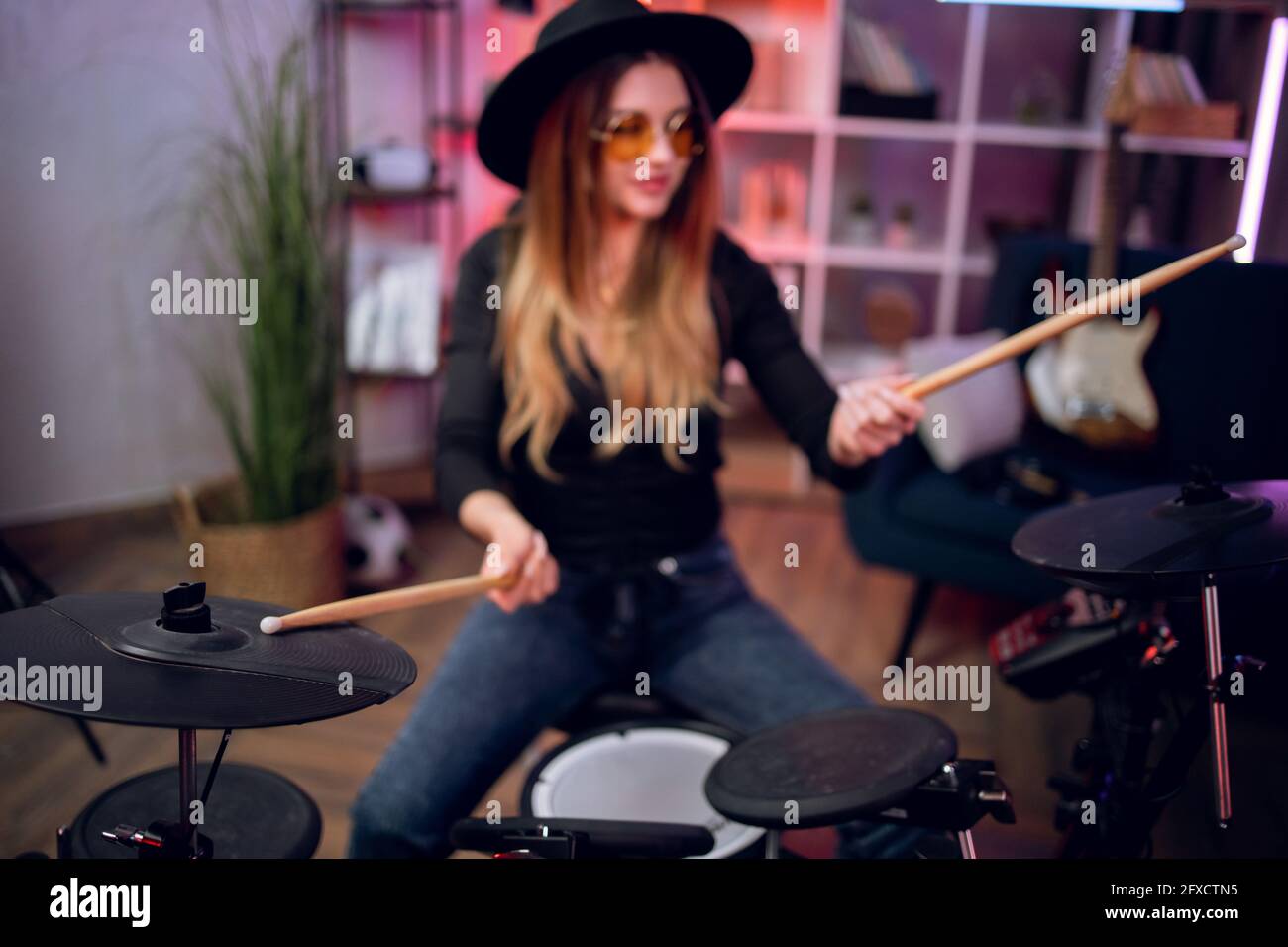 Talented female musician practising in playing electronic drums in studio. Attractive woman rehearsing alone indoors. Enjoyment from favorite hobby. Stock Photo