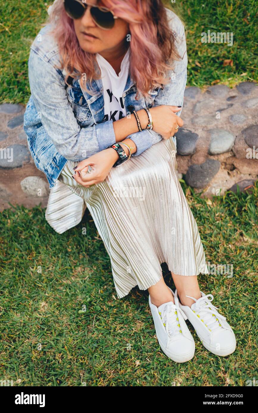 Seated modern independent woman, with pink hair, dark glasses, silver-gold  skirt and white sneakers. Hipster woman Stock Photo - Alamy