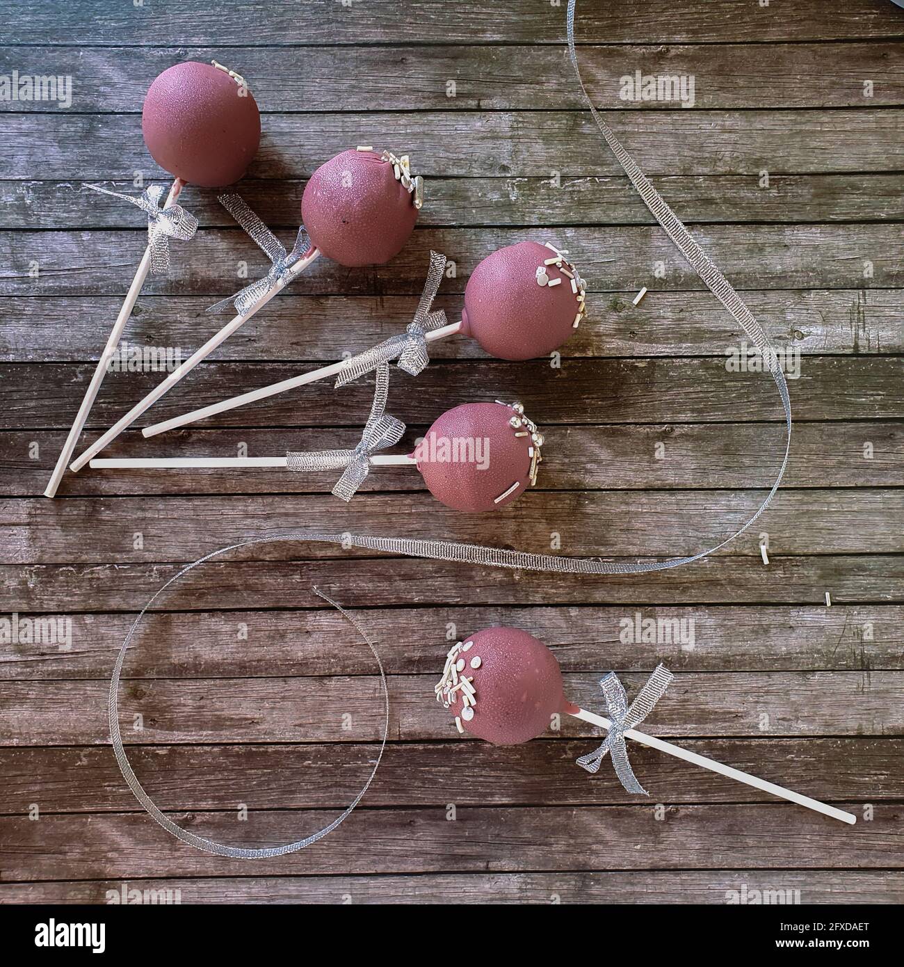Five pink cake pops laying on wooden table with white tape and bow Stock Photo
