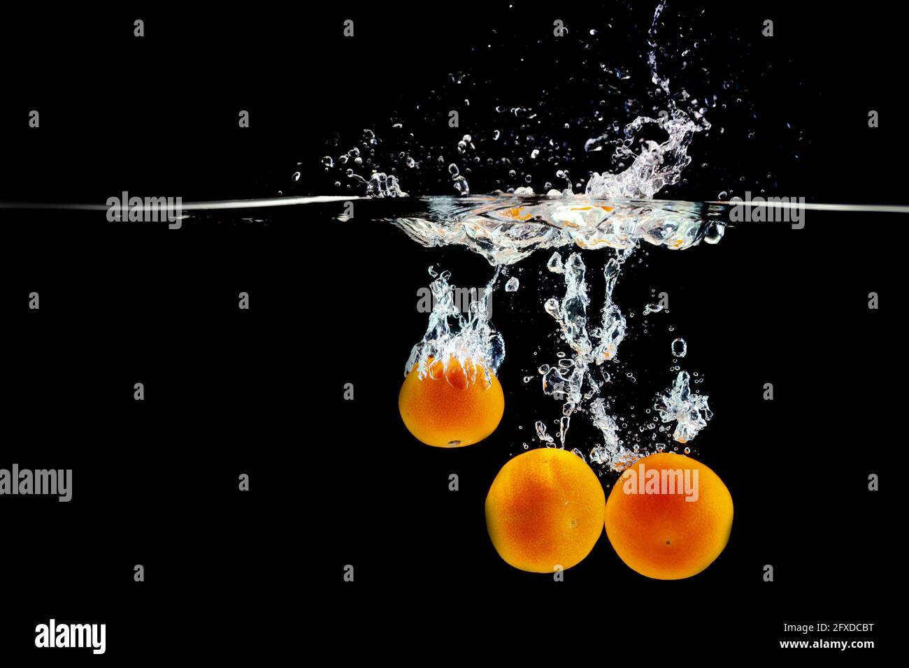 three juicy tangerines in water on a black background Stock Photo