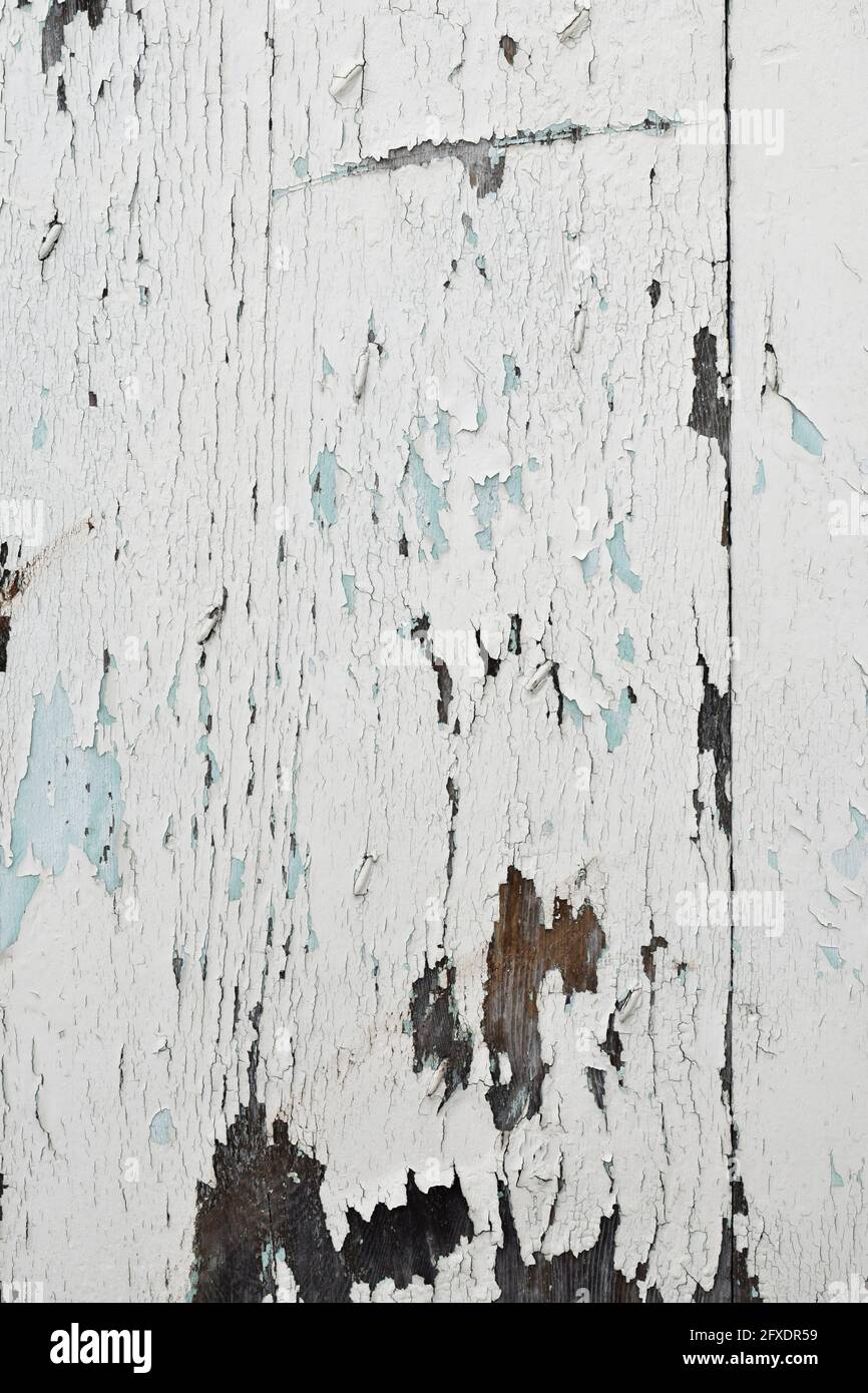 Peeling white paint exposes previous layers of brown and blue on an old garage door. Stock Photo