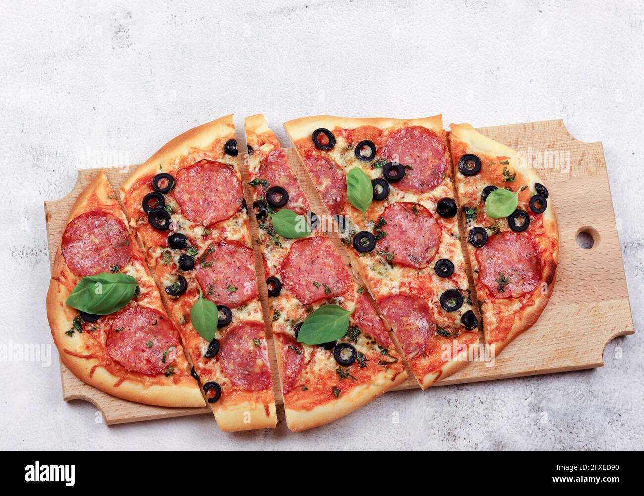 Sliced roman square pizza with cheese, sausage, olives and tomatoes on a round wooden cutting board on a light gray background. Top view, flat lay Stock Photo