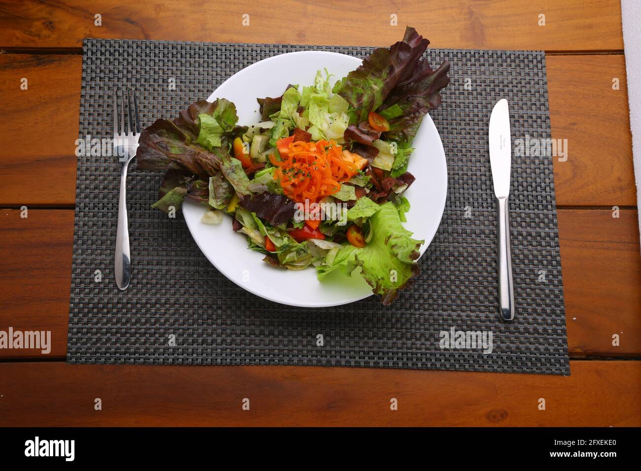 Dark Leafy Green Veg Salad,healthy leafy salad  arranged in a white plate  with grey table mat and serving knife and fork with wooden background or te Stock Photo