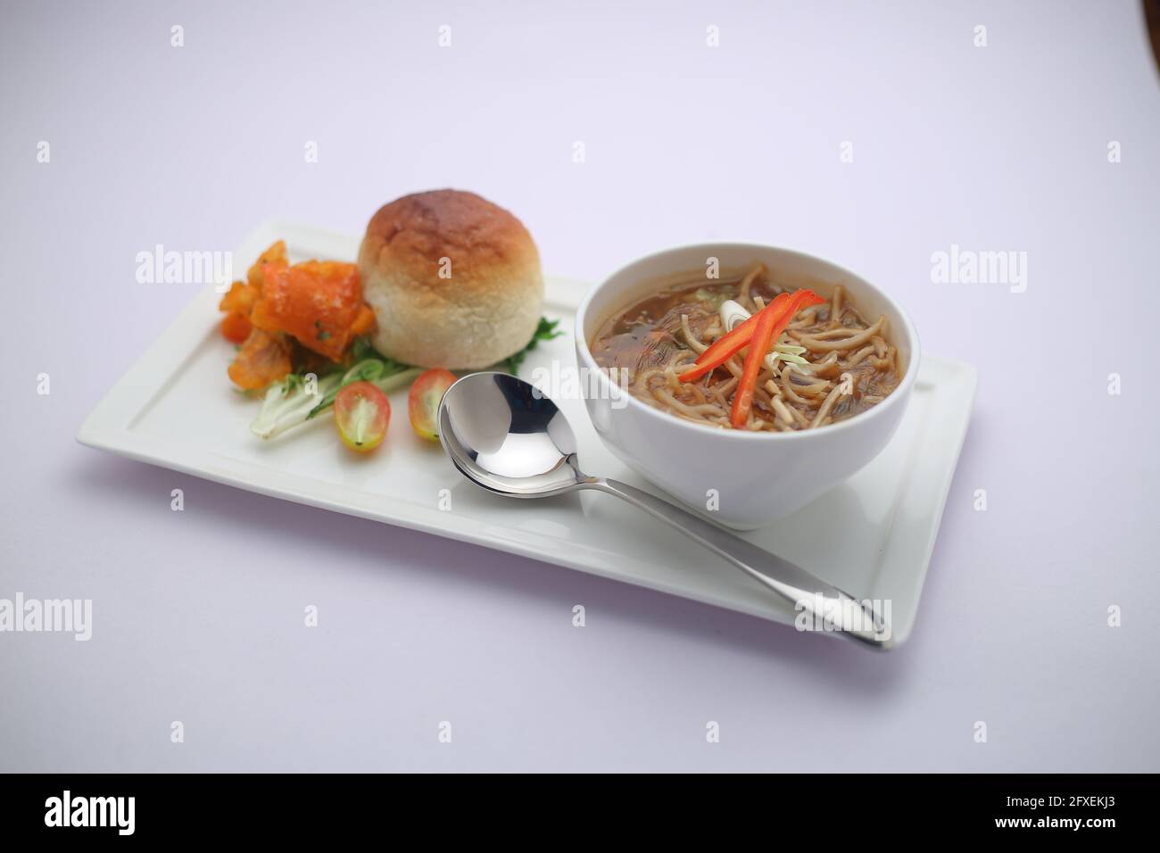 Chicken Manchow soup,garnished with vegetables and noodles arranged in a white bowl with white texture or background Stock Photo