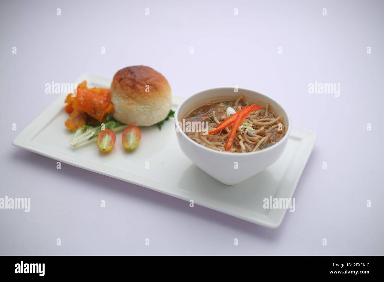 Chicken Manchow soup,garnished with vegetables and noodles arranged in a white bowl with white texture or background Stock Photo