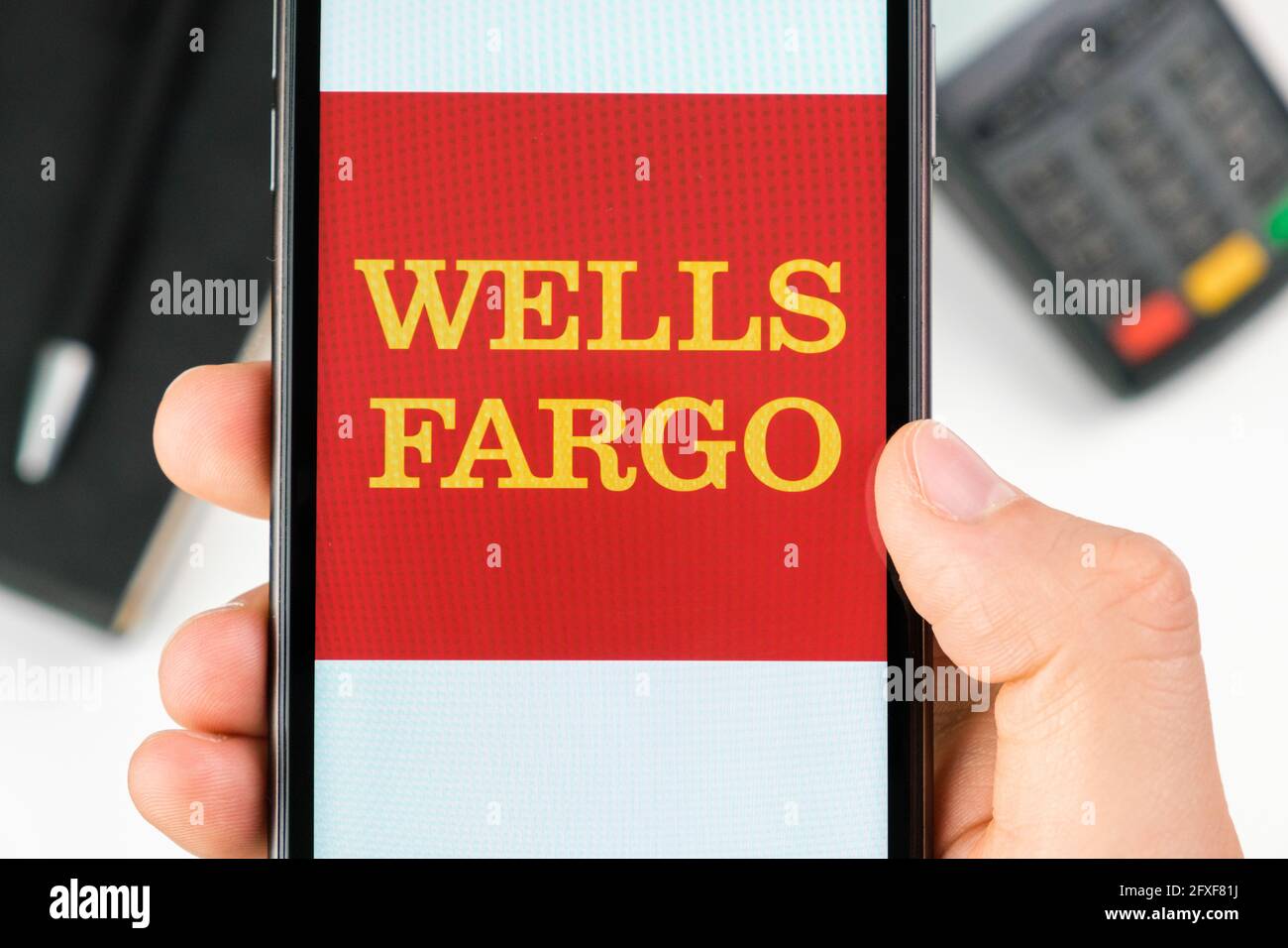 Wells Fargo bank logo on the smartphone screen in mans hand on the background of payment terminal, May 2021, San Francisco, USA Stock Photo