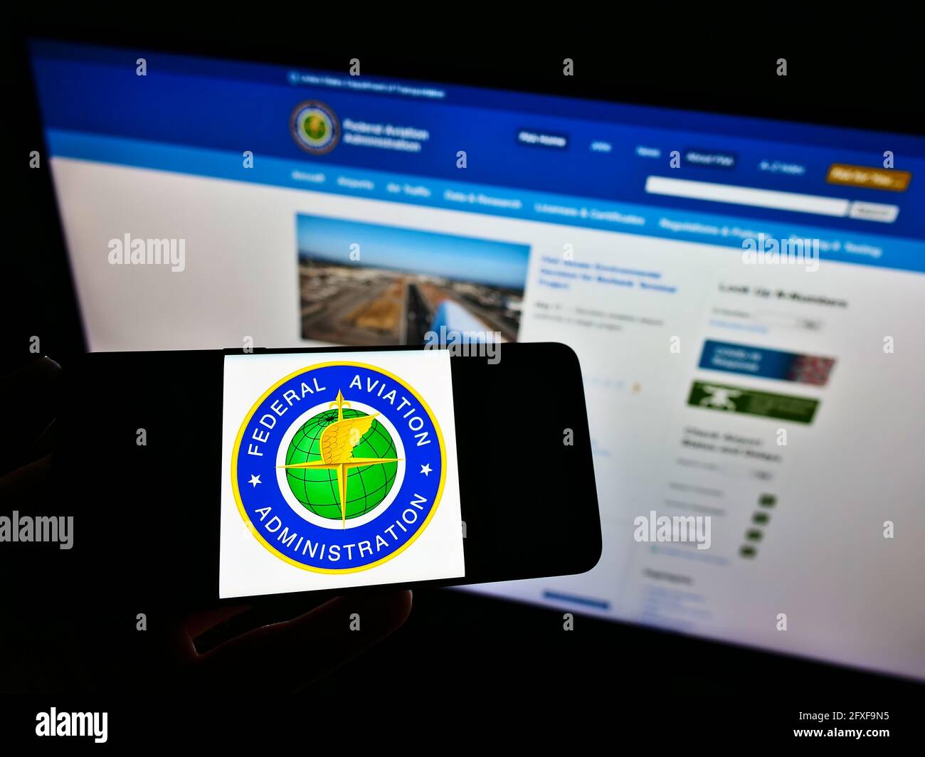 Person holding mobile phone with seal of American agency Federal Aviation Administration (FAA) on screen in front of webpage. Focus on phone display. Stock Photo
