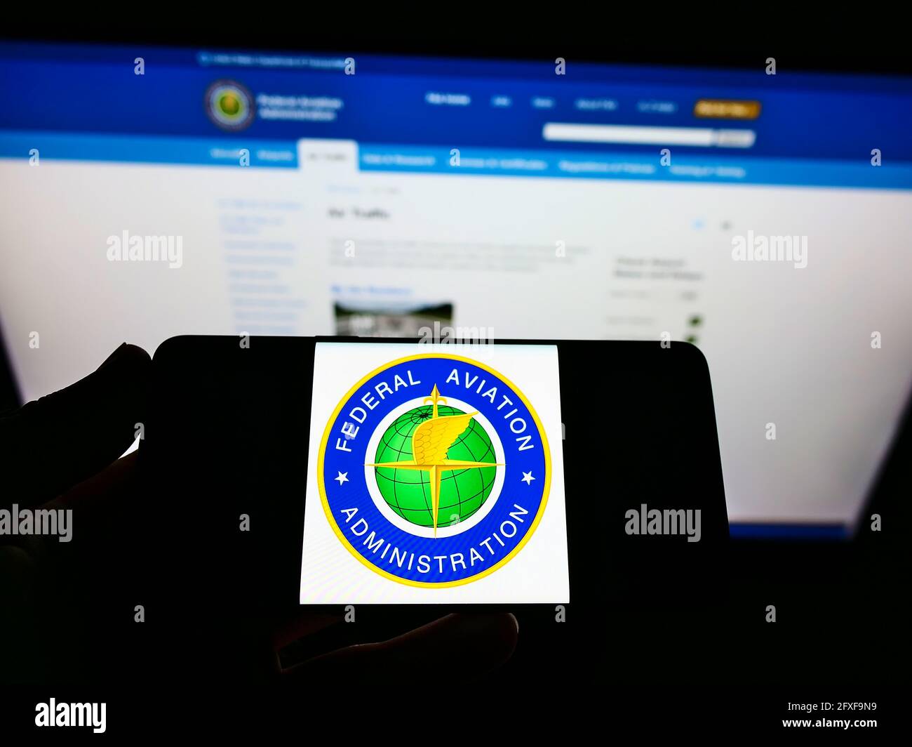 Person holding cellphone with seal of American agency Federal Aviation Administration (FAA) on screen in front of web page. Focus on phone display. Stock Photo