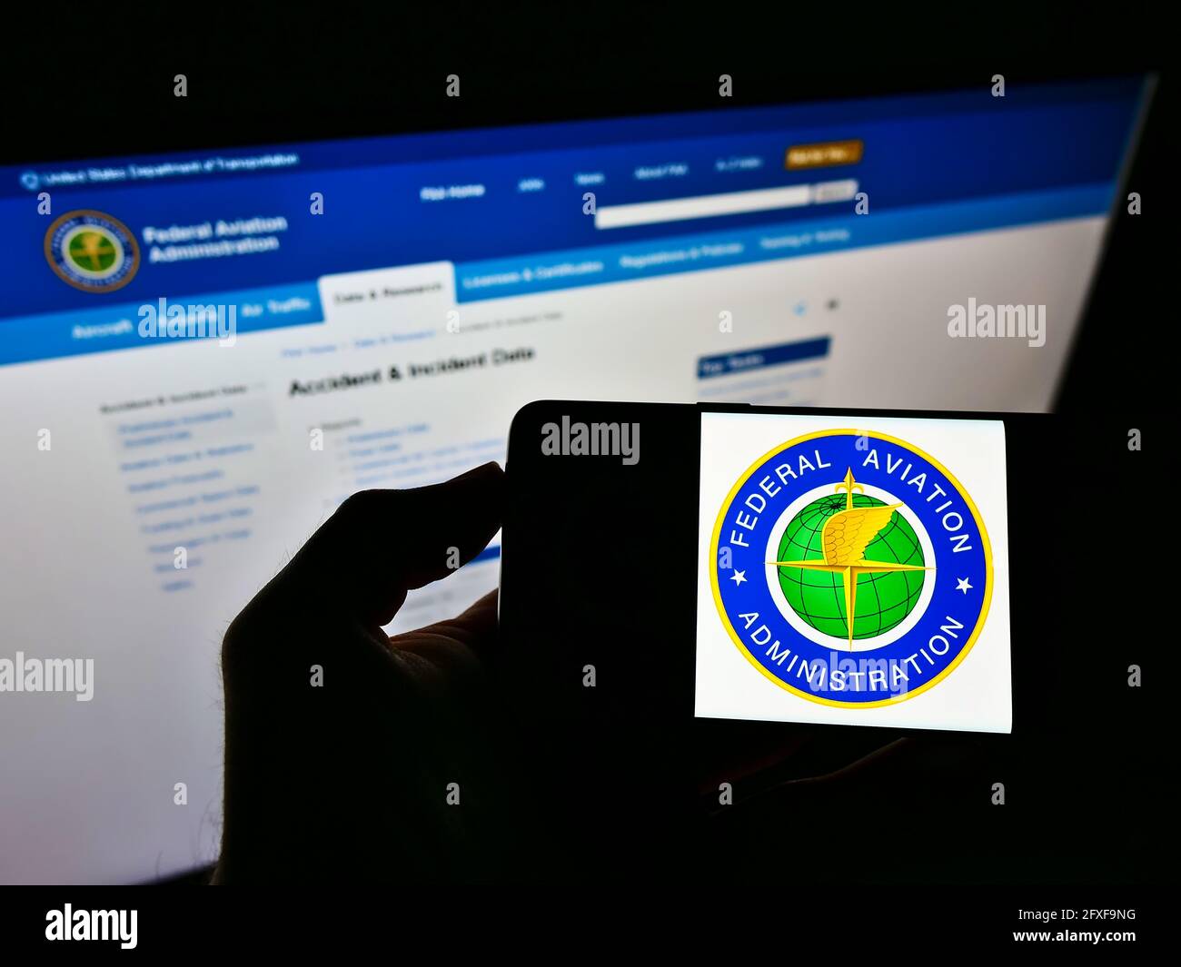 Person holding smartphone with seal of US agency Federal Aviation Administration (FAA) on screen in front of website. Focus on phone display. Stock Photo