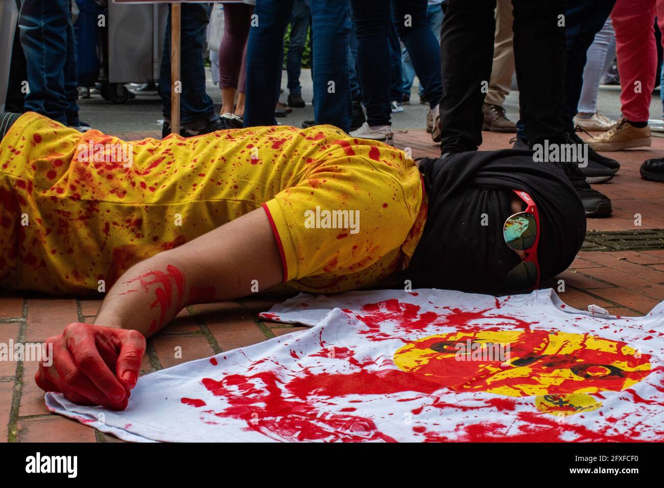 A demonstrator lies in the ground performing as it has been shot and wounded with a t-shirt of the Exito Supermarket stores as the supermarkets became focus on social media after videos showed that may have been used in torture cases involving police abuse of authority cases in a performing arts demonstration as artists and demonstrators protested against the government of president Ivan Duque Marquez and the abuse of force by police that leads to at least 40 dead across the country since the nation wide antigovernment protests started. In Medellin, Colombia on May 26, 2021. Stock Photo