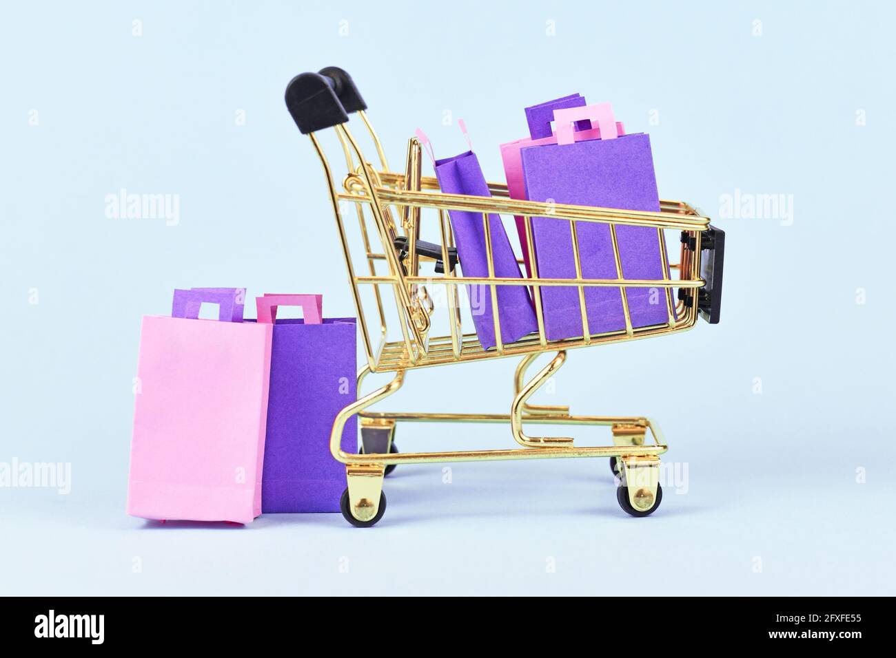 Golden shopping cart filled with pink and purple paper shopping bags on blue background Stock Photo