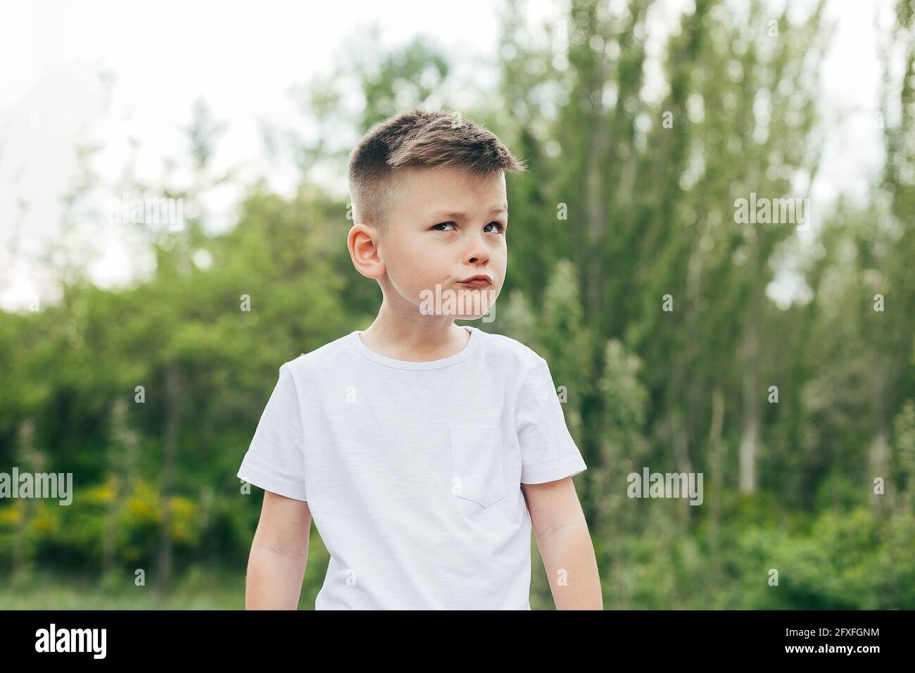 Portrait of funny cute boy in white Tshirt outdoor in park. Concept of