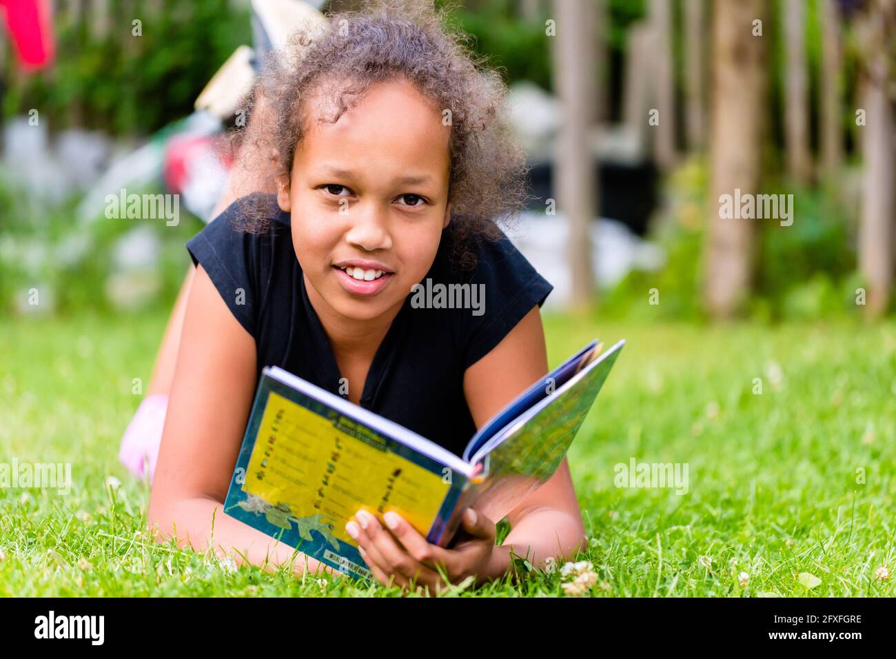 Black girl reading book on meadow lying in the grass Stock Photo - Alamy