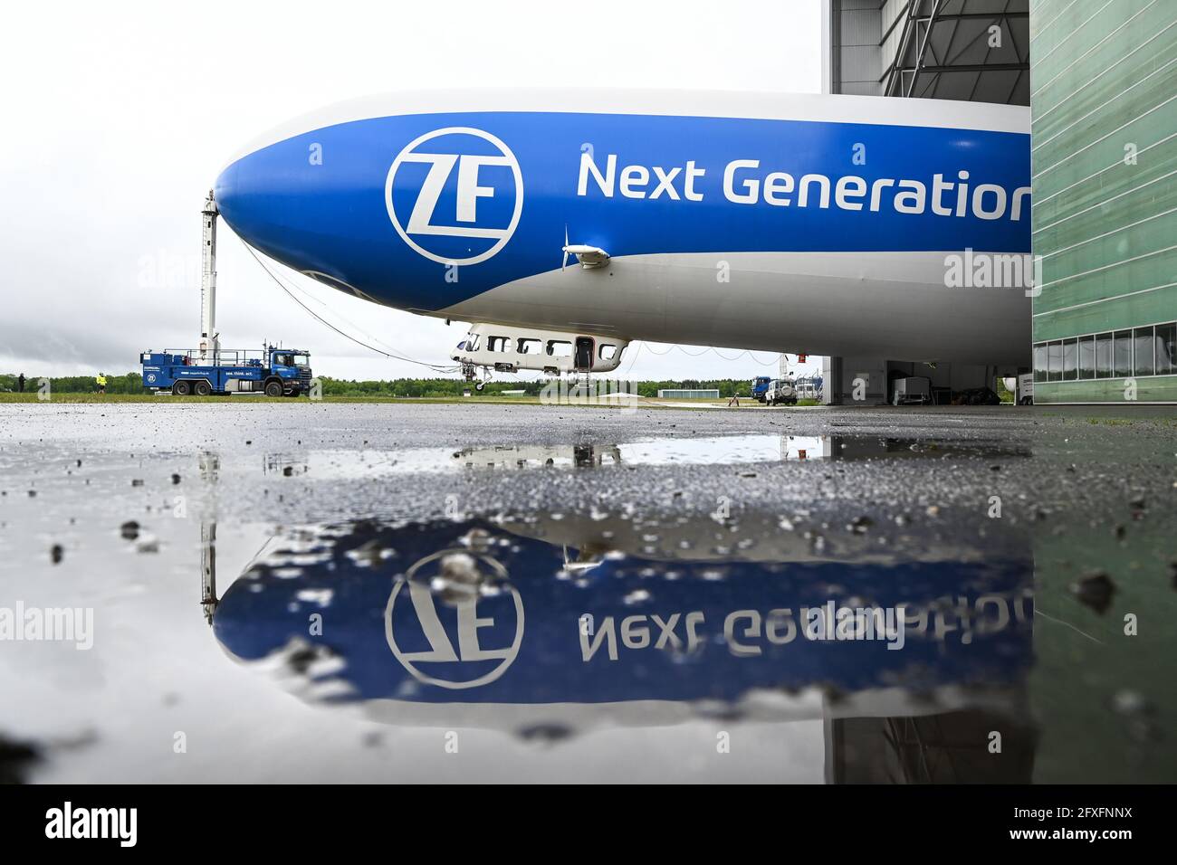 Friedrichshafen, Germany. 27th May, 2021. The Zeppelin NT (New Technology) is pulled out of the hangar by a truck so that the airship can take off for its press flight in the afternoon. The Zeppein itself is reflected in a puddle in front of the hangar. The Zeppelin NT will start its season on Friday, 28.05.2021. Credit: Felix Kästle/dpa/Alamy Live News Stock Photo