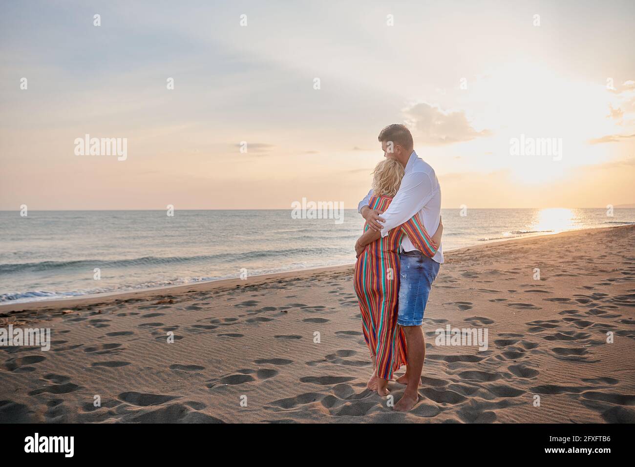 Woman and man hugging each other as they watch the sunset on the beach ...