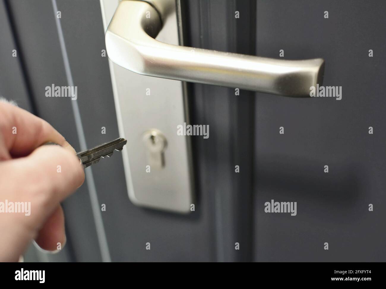 A hand holding a key for inserting a key into the door lock. Unlocking