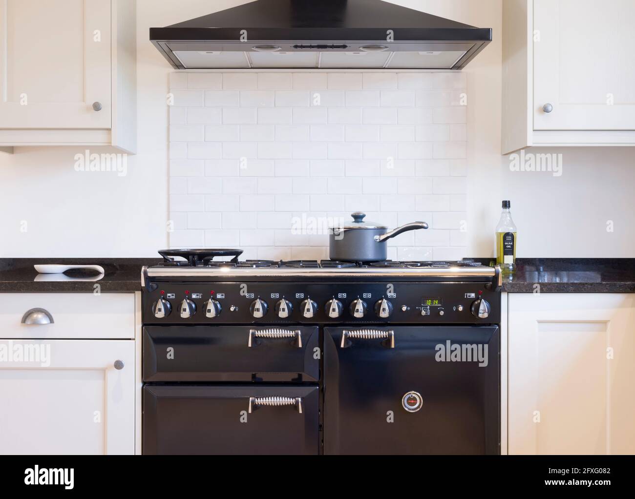 Black and white kitchen design. Painted wood modern kitchen with black enamel range cooker and chimney hood. UK shaker style kitchen remodeling Stock Photo