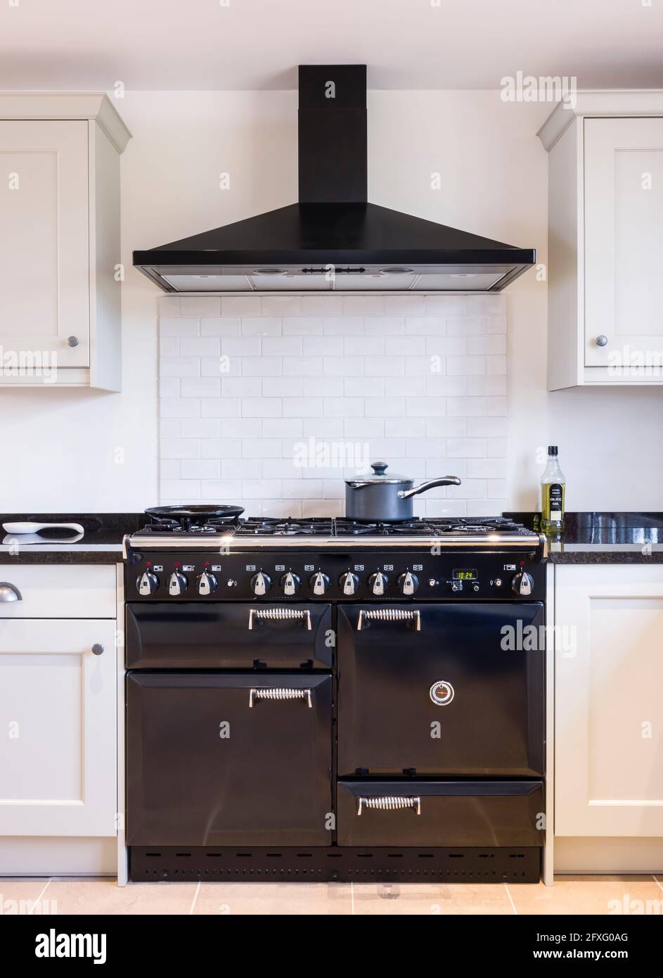Black enamel oven range cooker with chimney hood in a modern kitchen with shaker style painted wood units in neutral off white. UK farmhouse kitchens Stock Photo
