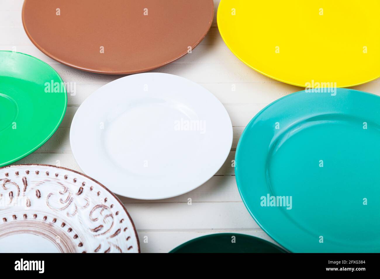 Empty multicolored plates on a wooden background, top view. Stock Photo