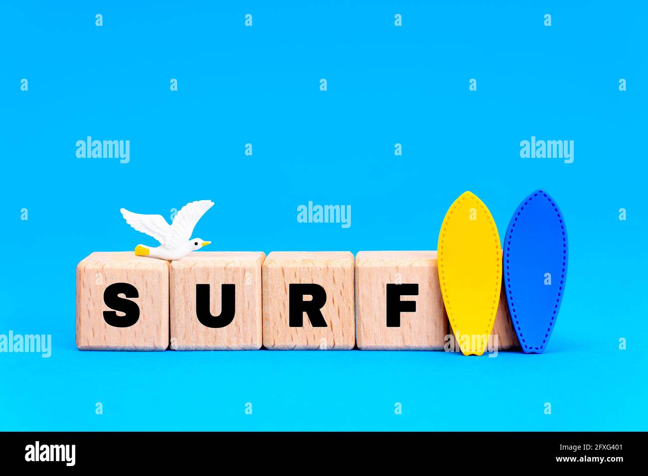 Word SURF made of wooden alphabet blocks with two surfboards figurines and a toy seagull on blue background. Stock Photo
