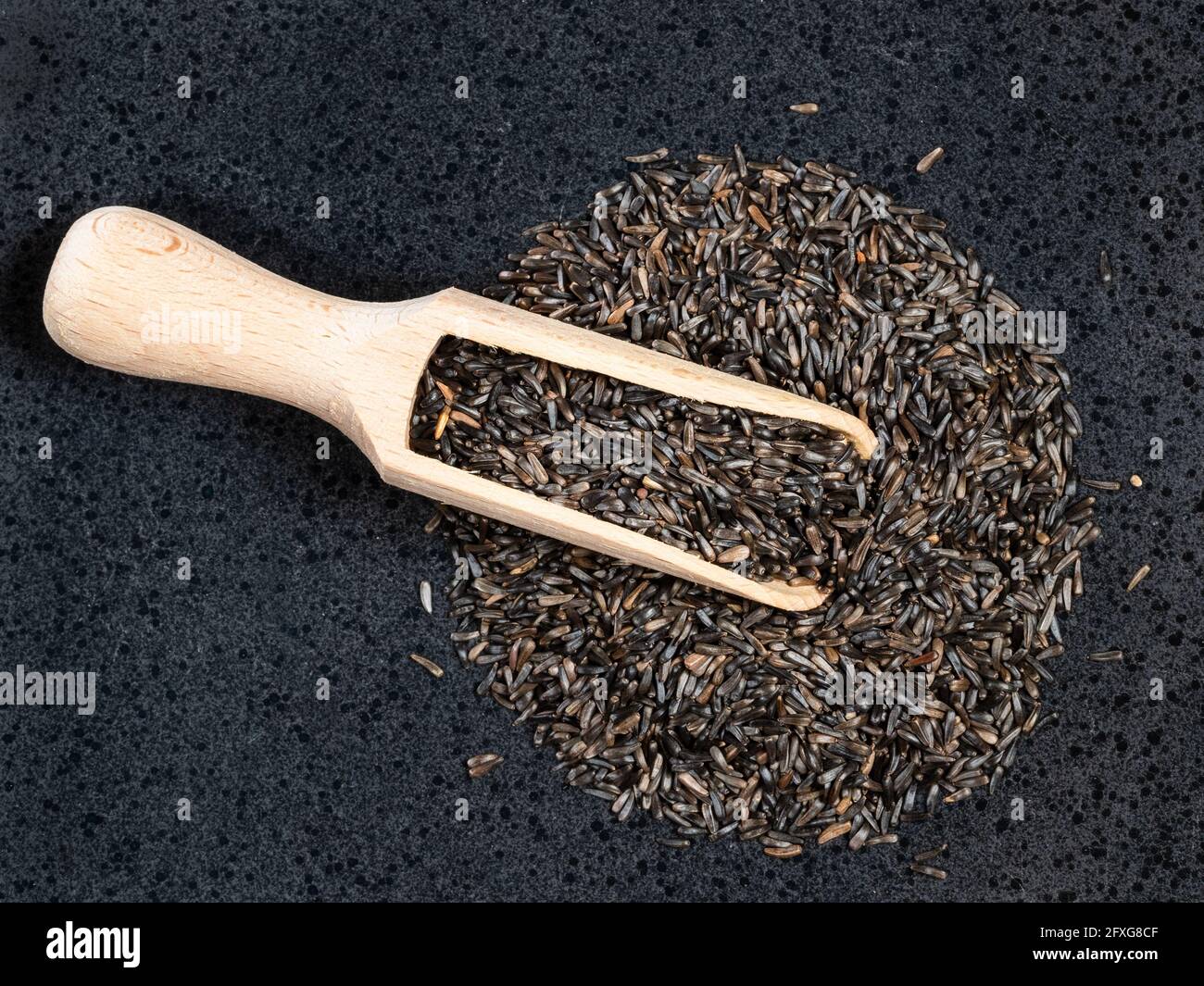 top view of wood scoop on pile of niger seeds (Guizotia Abyssinica) on black plate Stock Photo