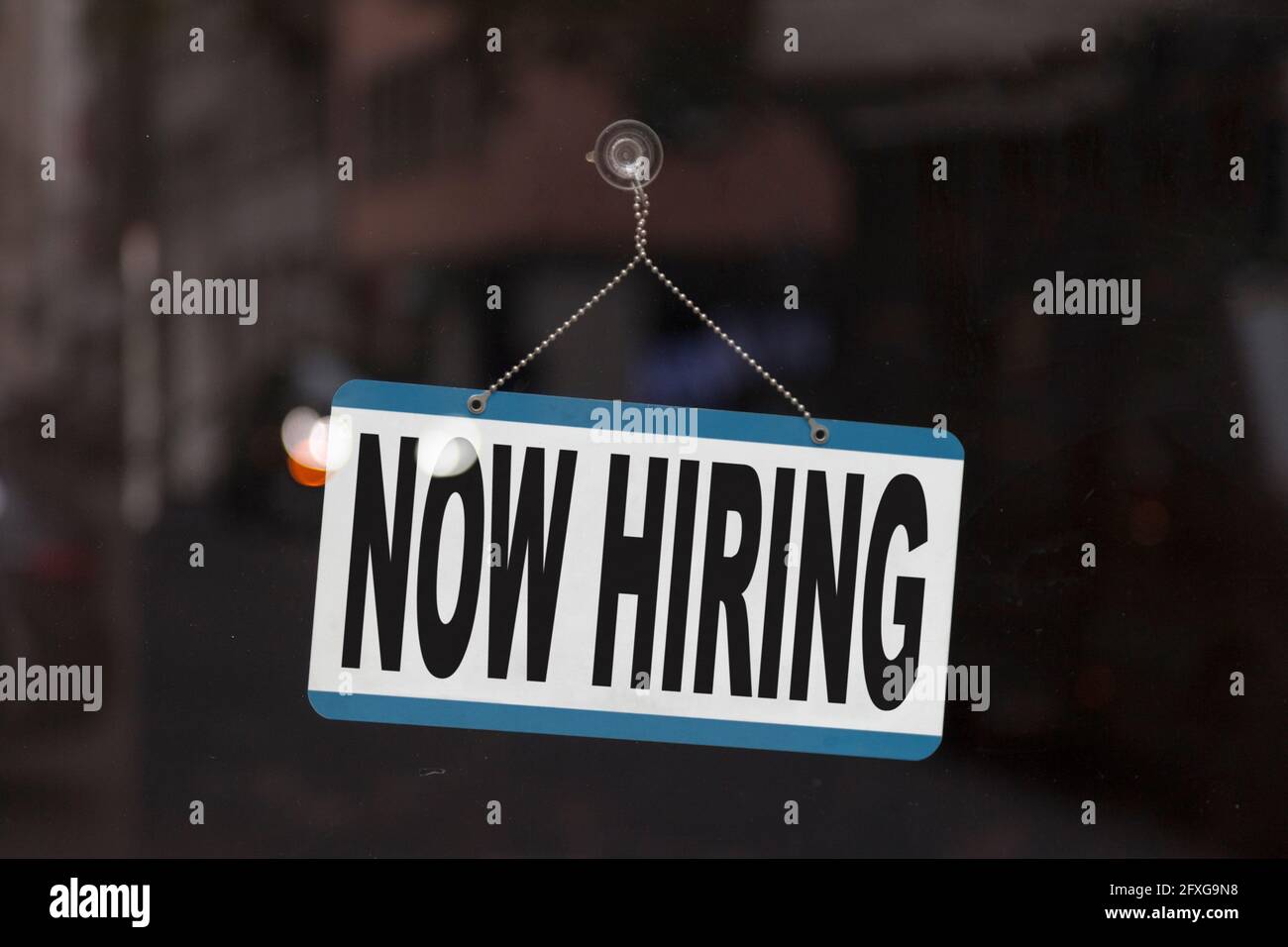 Close-up on a sign in the window of a shop displaying the message: Now hiring. Stock Photo