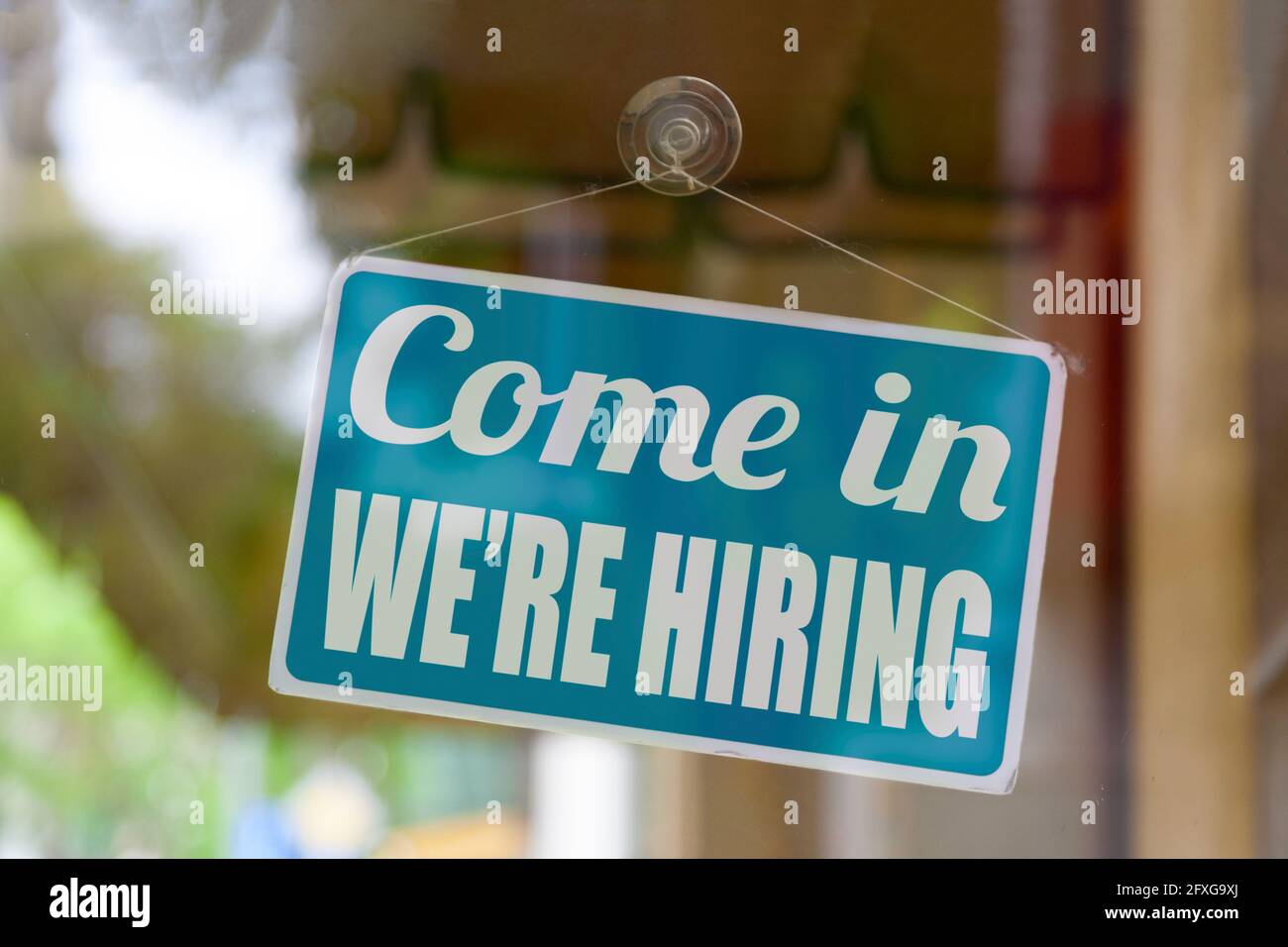 Close-up on a blue sign in the window of a shop displaying the message: Come in we're hiring. Stock Photo