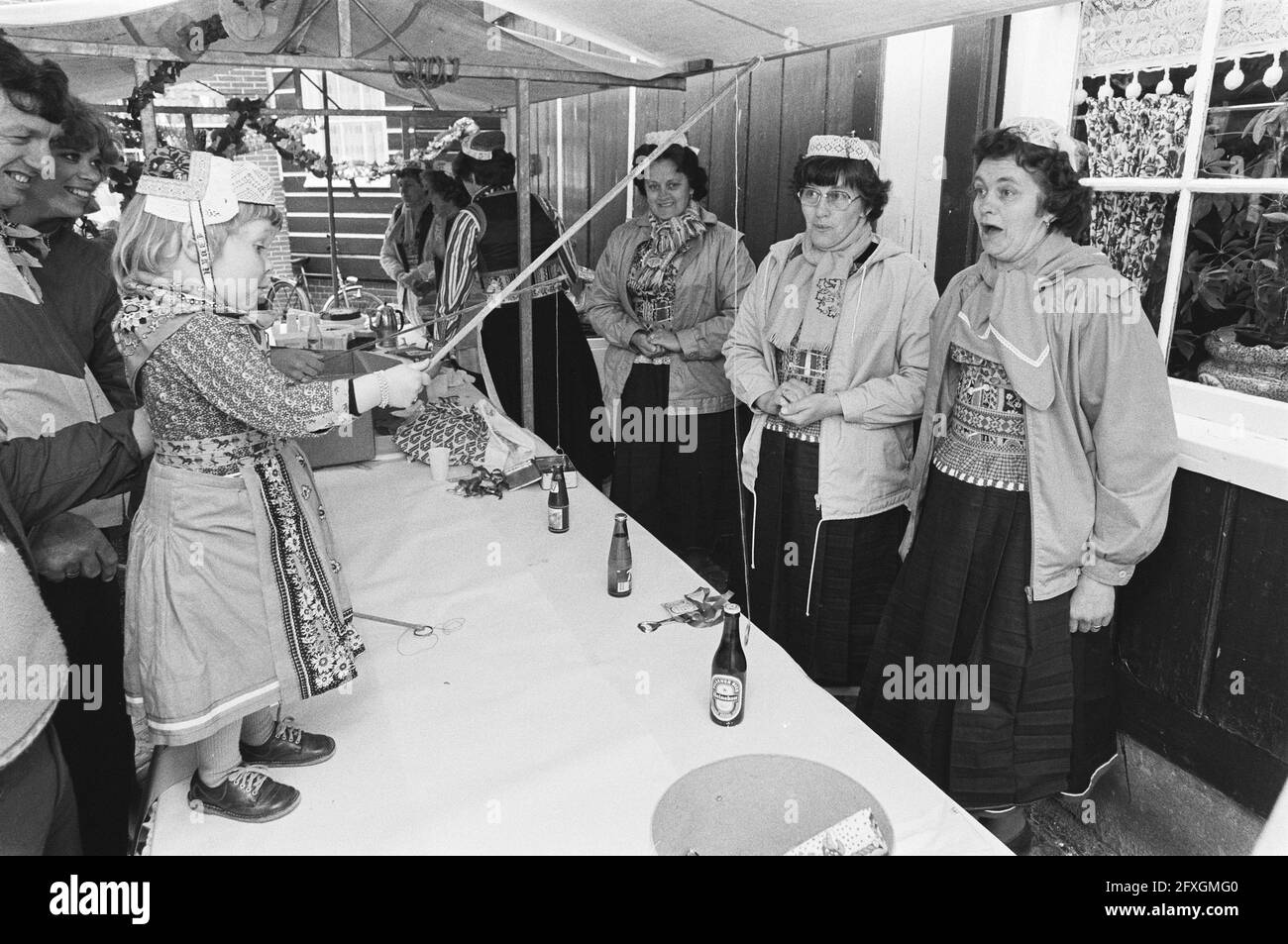 Celebrating Queen's Day in Amsterdam and Marken. Girl in traditional costume in Marken fishes for a bottle of drink, April 30, 1982, KONINGINNEDAG, The Netherlands, 20th century press agency photo, news to remember, documentary, historic photography 1945-1990, visual stories, human history of the Twentieth Century, capturing moments in time Stock Photo