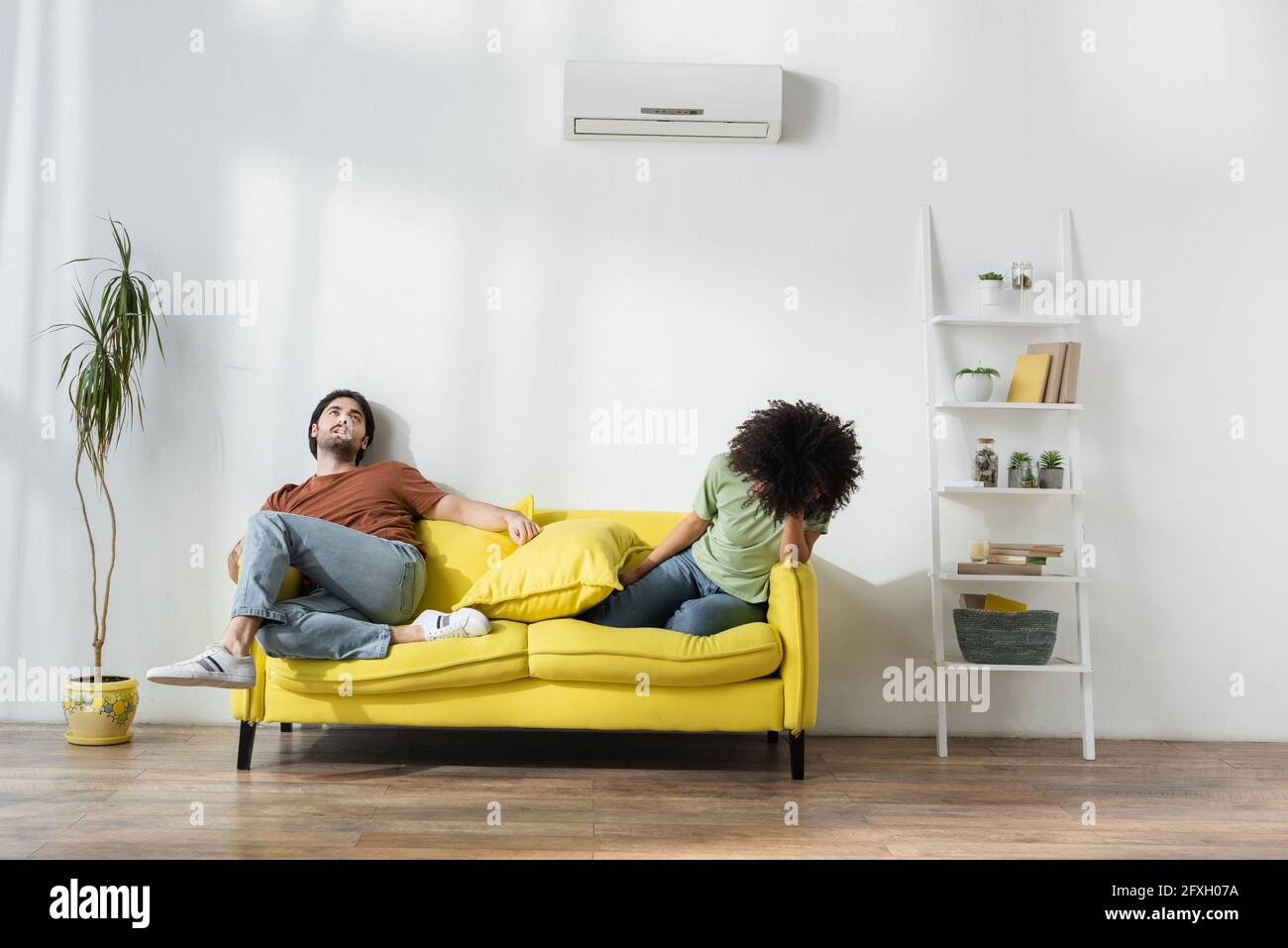 exhausted interracial couple sitting on sofa and suffering from heat in summer Stock Photo