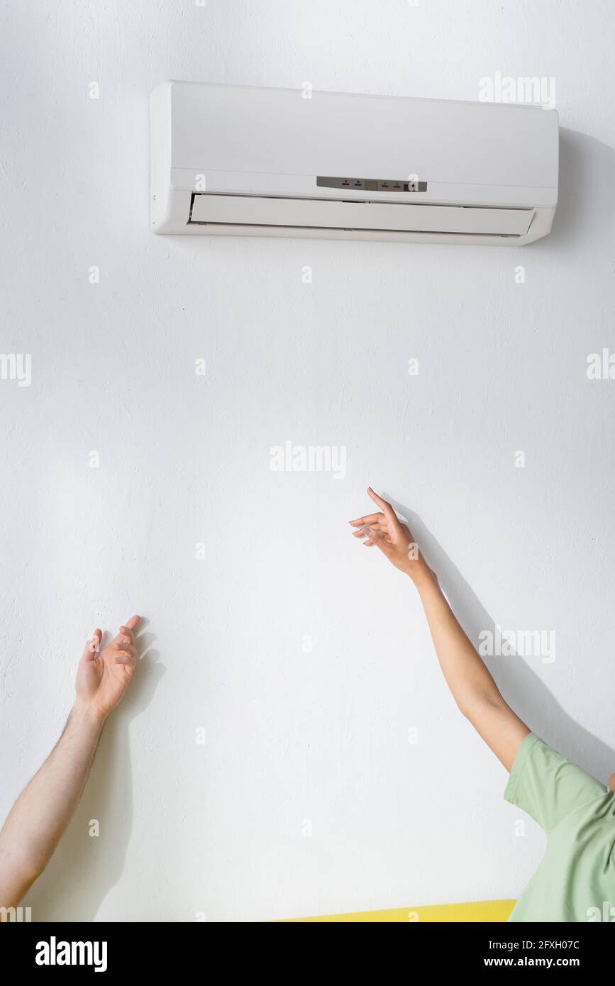 cropped view of multiethnic couple reaching air conditioner while suffering from heat in summer Stock Photo