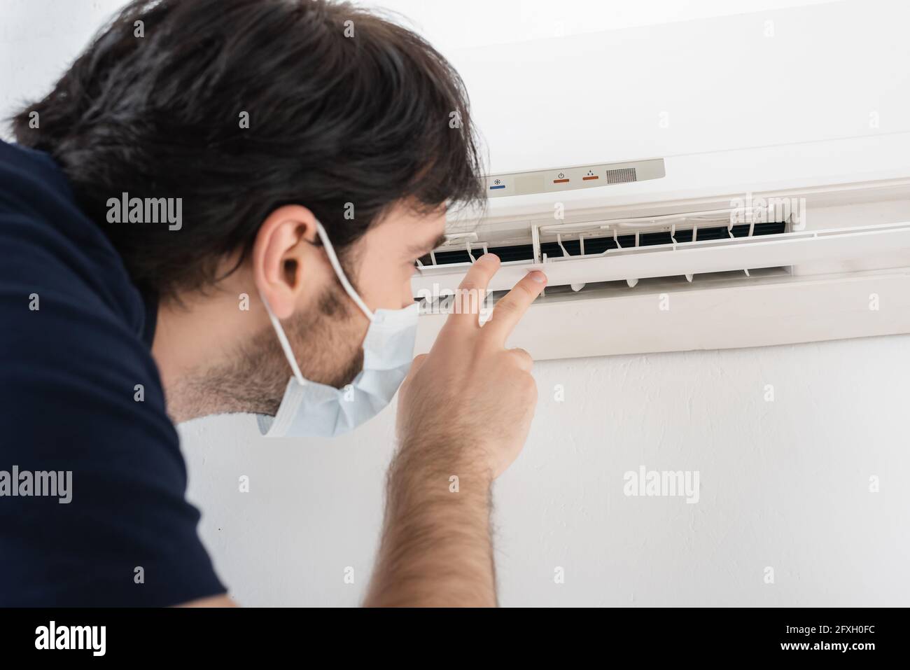 handyman in medical mask gesturing near air conditioner while checking