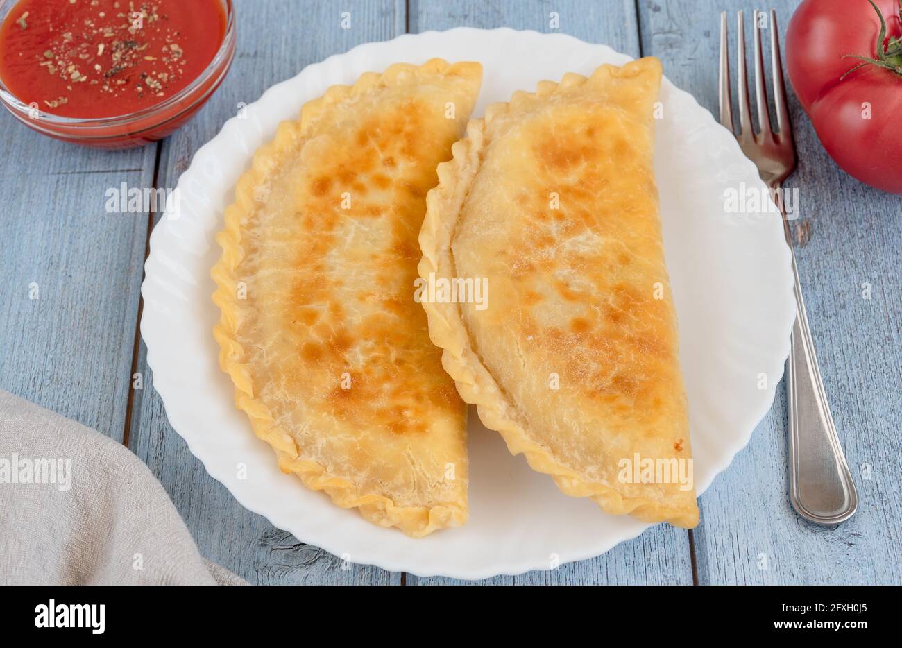 Fried pies with meat - Chebureks in a plate, a bowl with tomato sauce Stock Photo