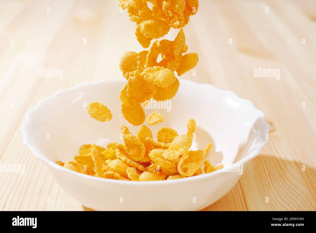 cereals falling in a white bowl on a wooden table Stock Photo