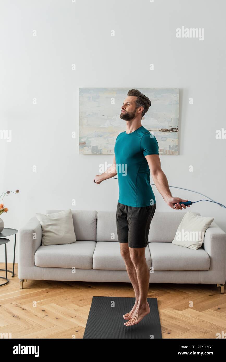 full length view of sportive man jumping with skipping rope at home Stock Photo