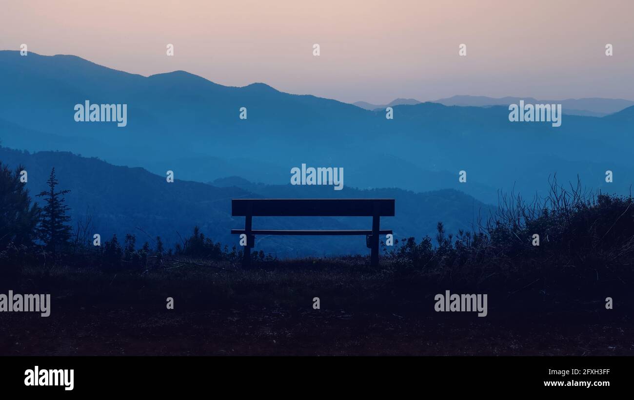 Empty wooden bench in mountain area during sunset or sunrise twilight hours. Nature tranquility landscape, no people Stock Photo