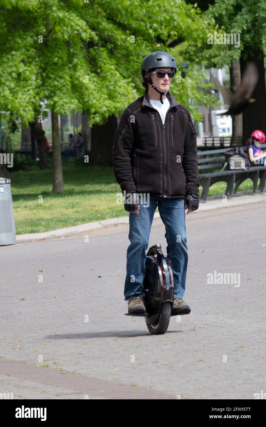 On a Spring day, a man wearing a hemet rides an electric unicycle in Flushing Meadows Corona Park in Queens, New York City. Stock Photo