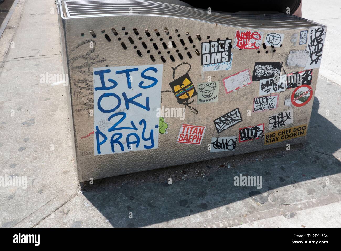Stickers and graffiti on a bench & subway grating on Steinway Street in Astoria, Queens, New York City Stock Photo