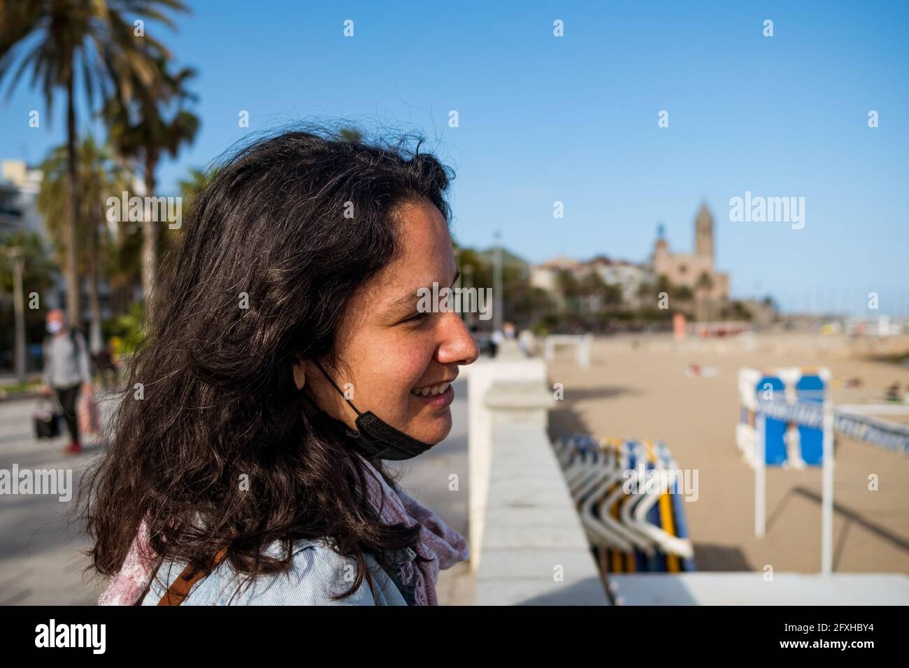 a young smiling tourist woman looking at the empty beach in Sitges during tourist season, a Spanish Beach Resort in Catalonia, Spain. Spanish tourism Stock Photo