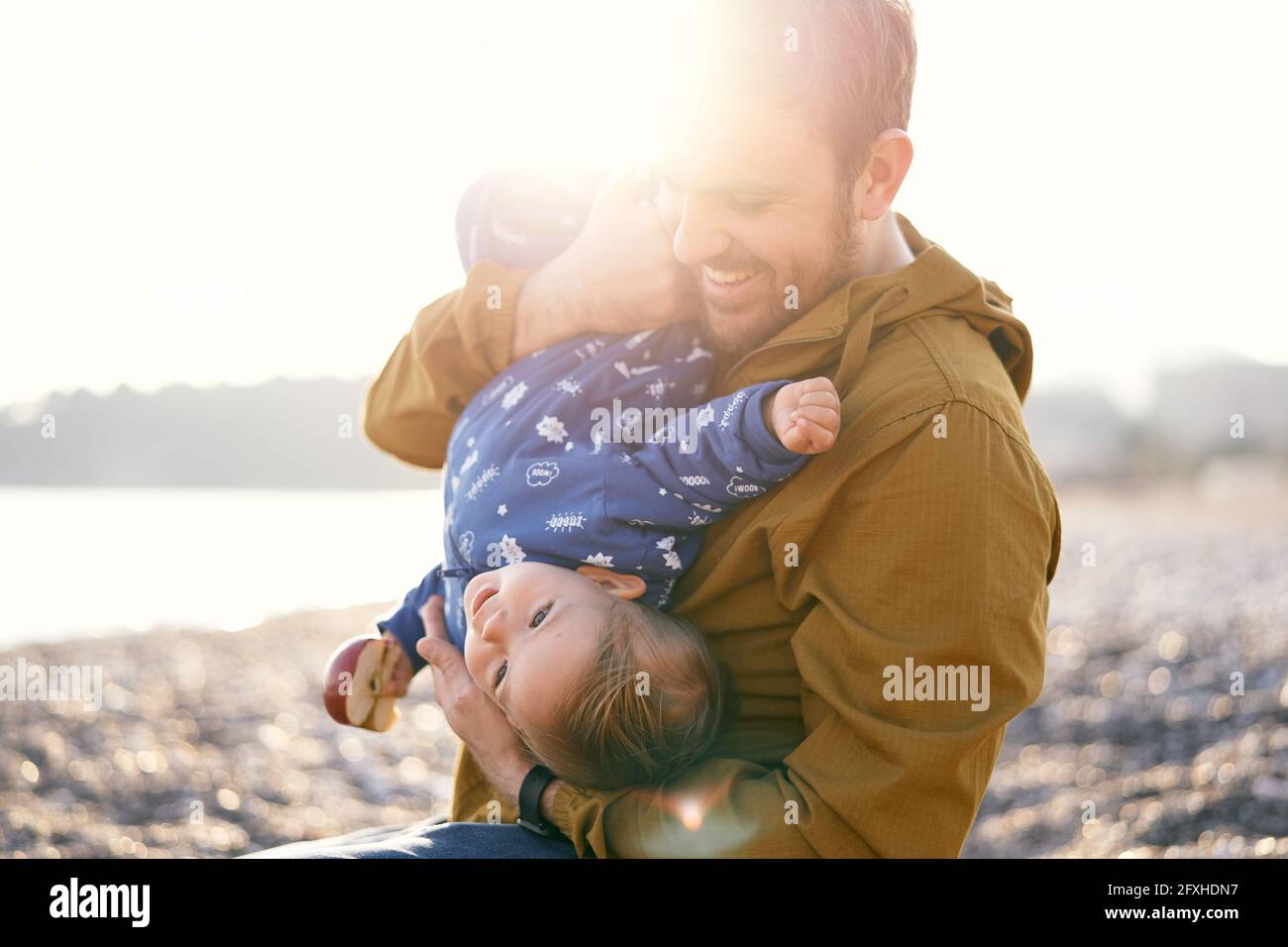 Smiling dad in the bright sunlight hugs a small child in a blue ...